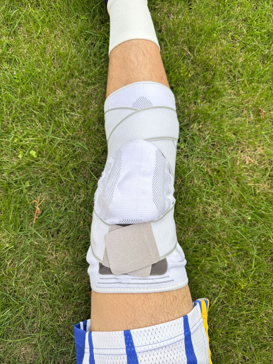 Person wearing a white TEVANLY Adjustable Compression Knee Brace outdoors on grass.