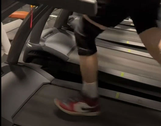 Runner wearing a black knee brace while exercising on a treadmill at the gym.